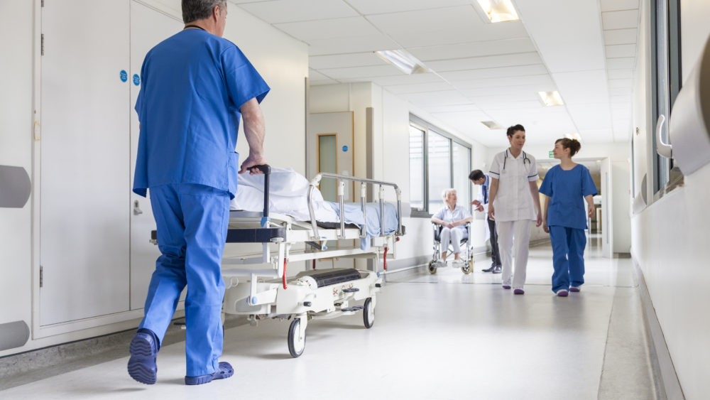 Doctors Hospital Corridor Nurse Pushing Gurney Stretcher Bed Male nurse pushing stretcher gurney bed in hospital corridor with doctors & senior female patient