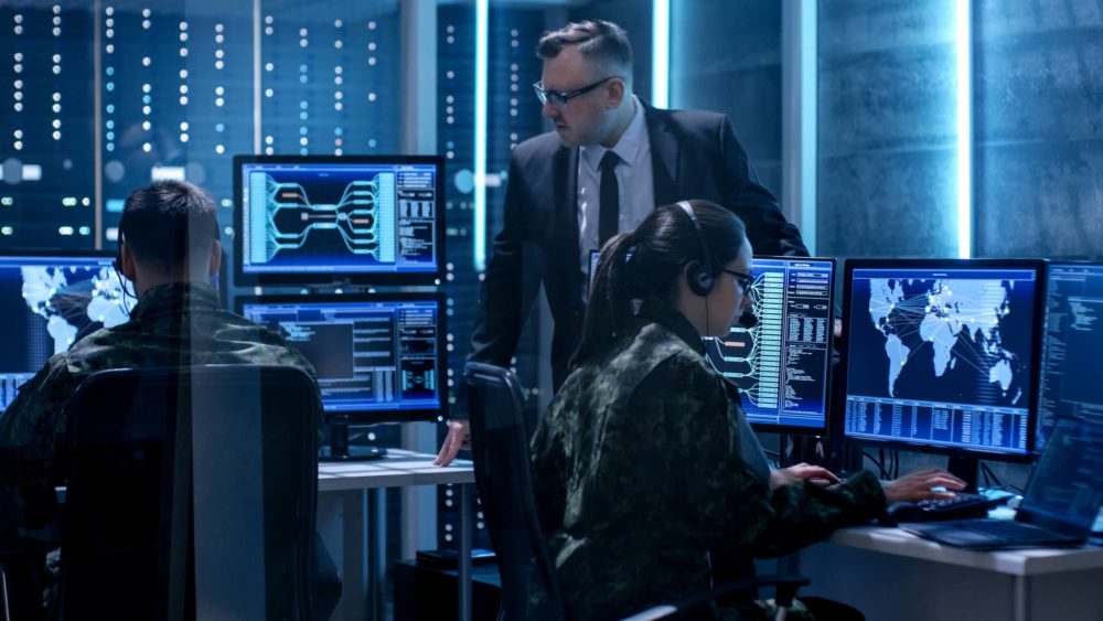 Team of Government Agents Tracking Fugitive with Boss’s Survillance in Big Monitoring Room Full of Computers with Animated Screens. Team of Government Agents Tracking Fugitive with Boss's Survillance in Big Monitoring Room Full of Computers with Animated Screens.